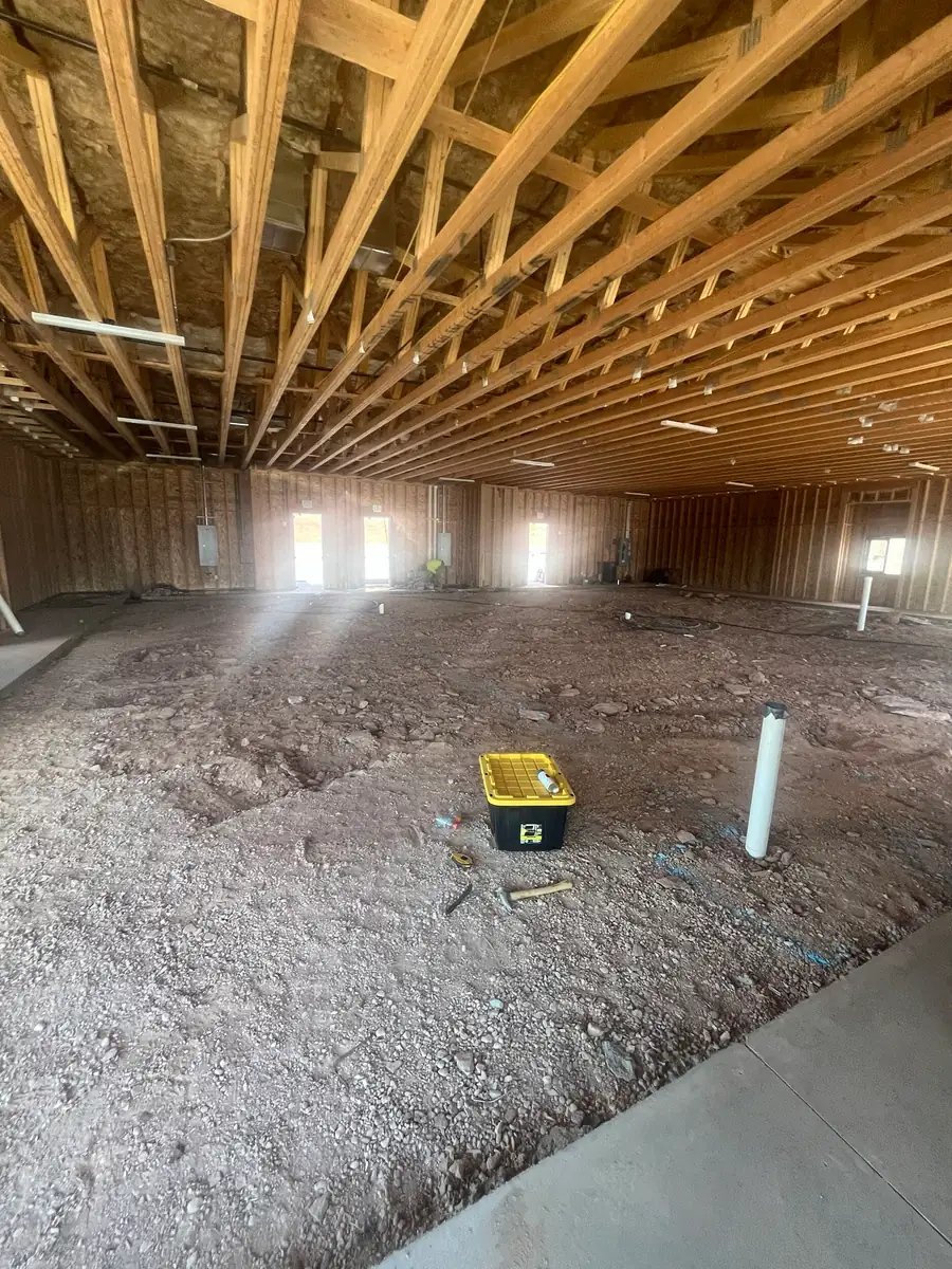 Wide interior view of the Agave Animal Hospital under construction: exposed wood roof trusses overhead, framed and sheathed walls, and a bare subgrade floor with several white pipe stub-ups standing in the dirt.