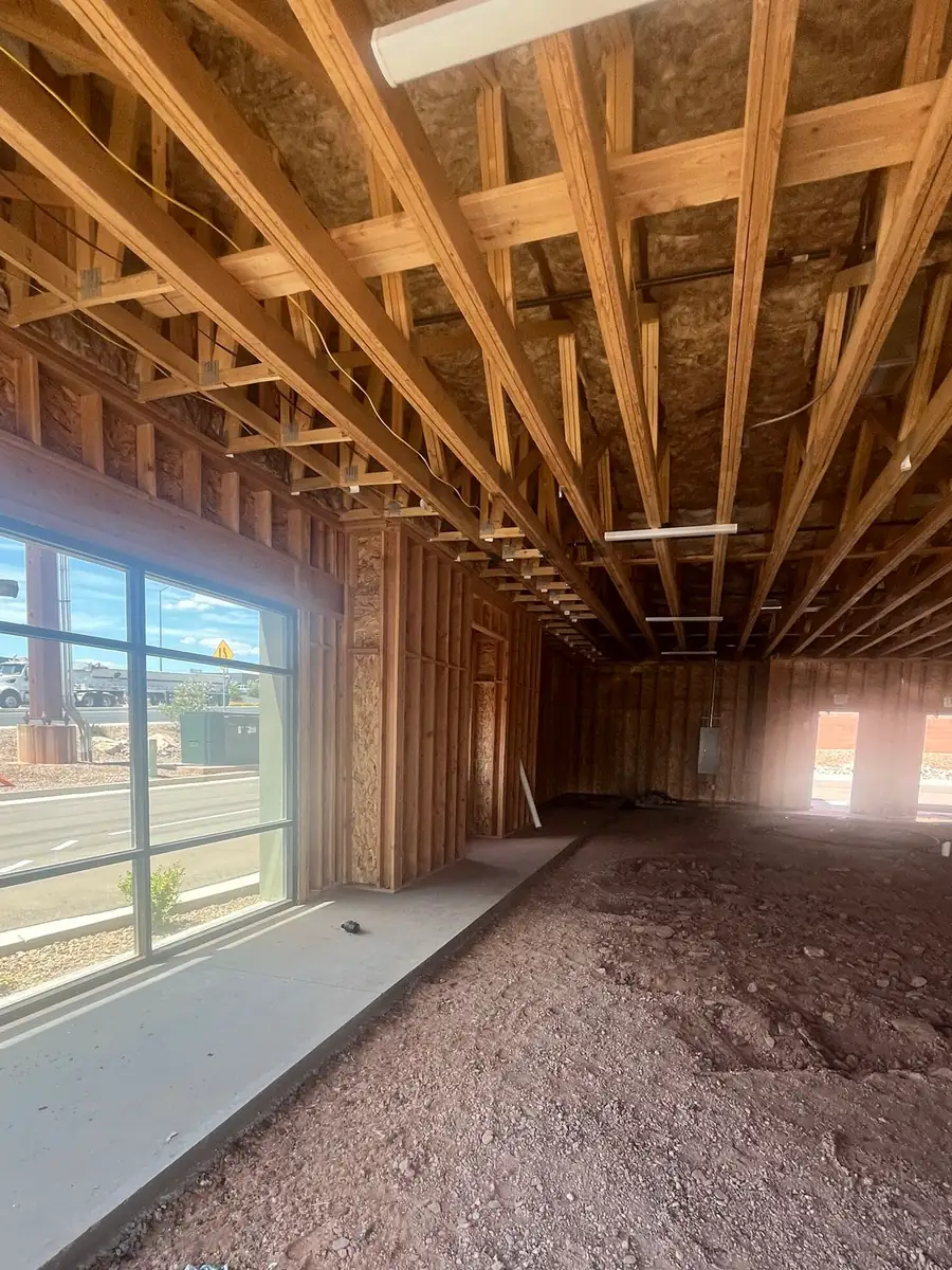 View from inside the Agave Animal Hospital building through a large storefront window onto River Road in St. George, Utah, with wood roof trusses overhead and part of the concrete floor already poured.