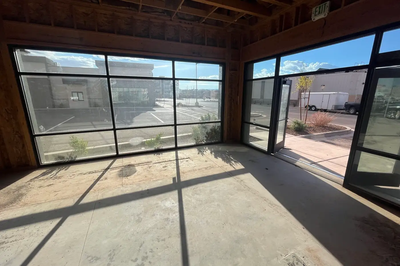 Sunlight pouring through a corner of storefront windows onto the bare concrete floor of the Agave Animal Hospital building, with one glass door propped open to a landscaped sidewalk outside.