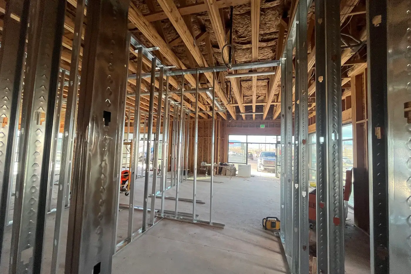 View between metal-stud walls toward a glass storefront door at the front of the Agave Animal Hospital building, with a folding table near the door and a pickup truck parked outside.